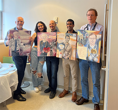 A group of doctors stand with Juliet Locke. The doctors are holding up portrait artwork.