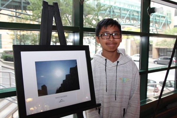 Younger teen wearing a white hoodie stands next to a framed image of the sky.
