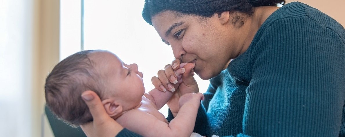 Close up of a mom holding an infant and kissing its hands in a hospital room