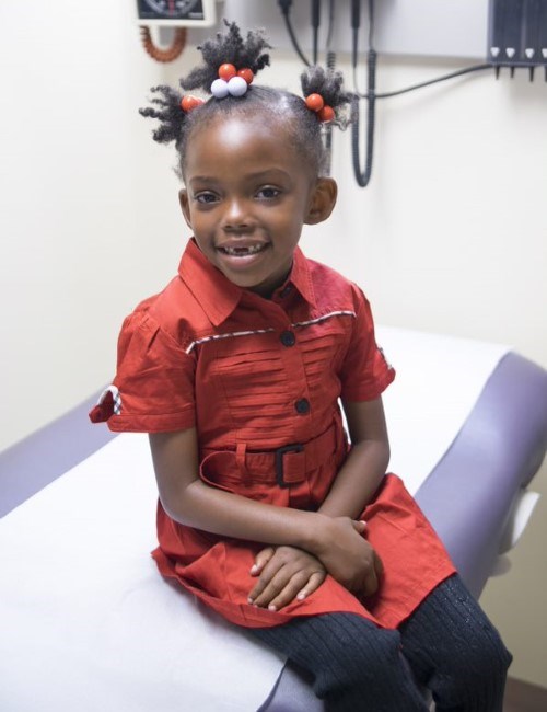 A young girl sitting on a medical examination bench smiling