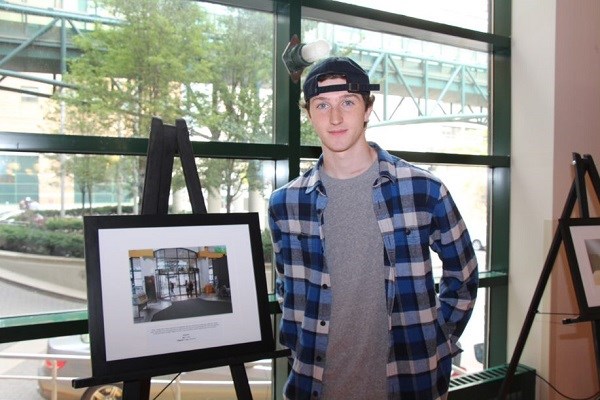 Teen stands next to framed photo of the SickKids revolving door.