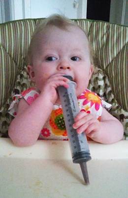 Baby sits in high chair with plastic syringe.