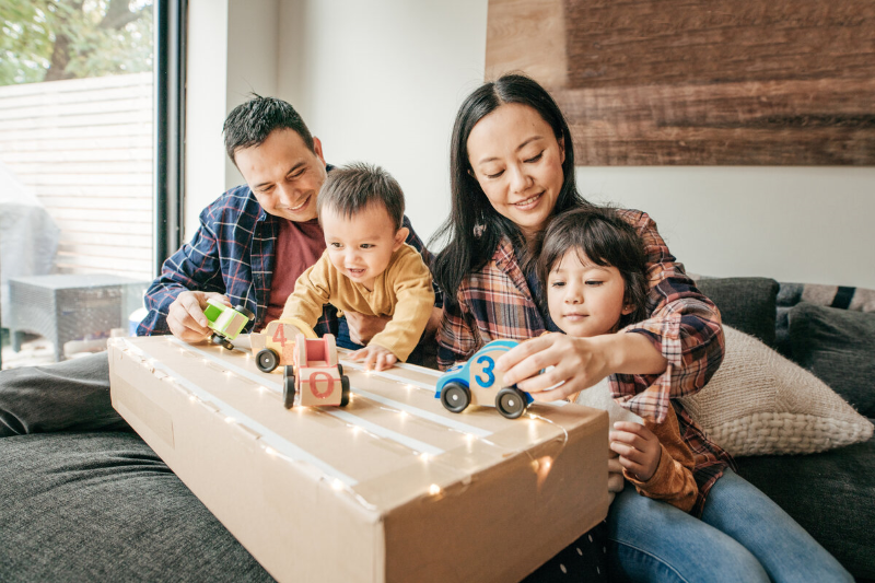 A young family sits together playing with toy cars.