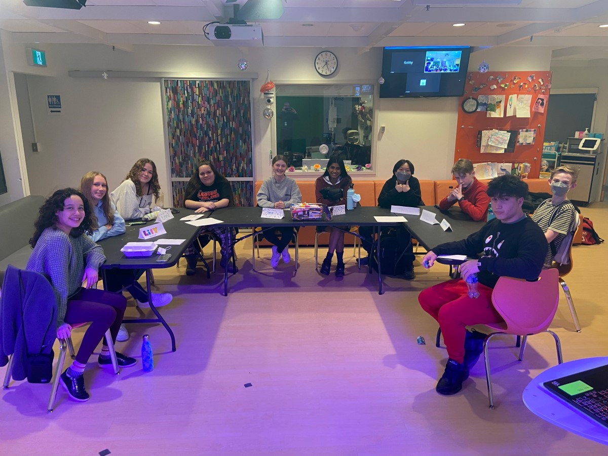 Ten people sit around a U-shaped table with papers and snacks, discussing at a patient advisory council meeting in a bright room.