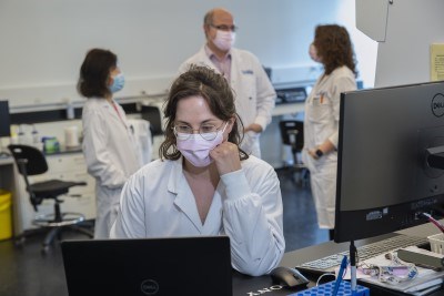 Sara Gordillo-Sampedro looking at her laptop screen. Flow Facility members are chatting in the background.