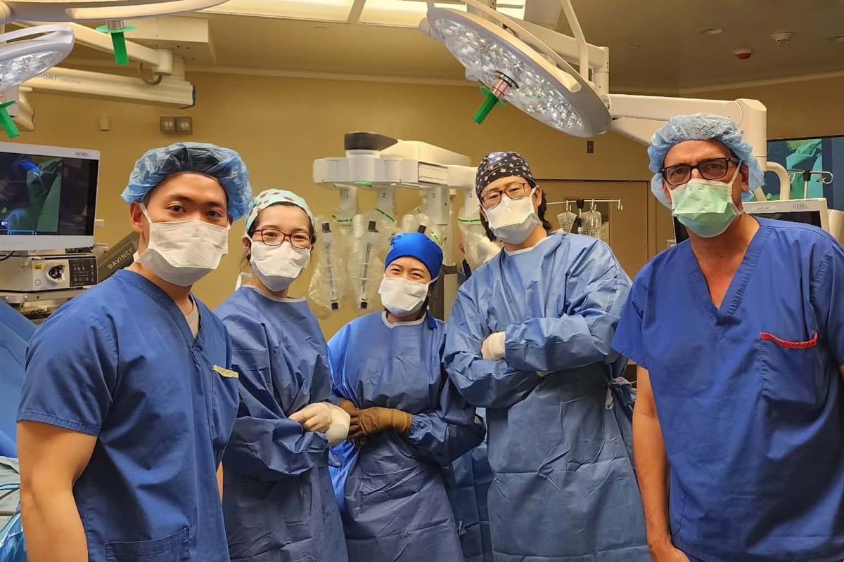  Five people wearing blue scrubs, masks and caps stand in the OR.
