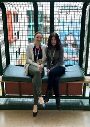 Two women sit side by side on a bench in the SickKids atrium.