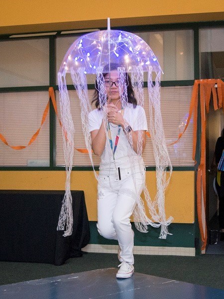 Adult dressed in white holding an umbrella over her head. The umbrella and has lights and tentacles.