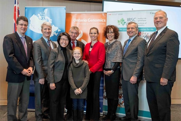 Group of formally dressed adults stand in front of an official backdrop, with one child in front.