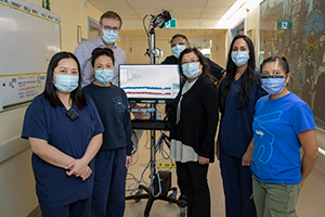 A team of physicians and EEG technicians gather around an EEG monitor.