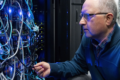 Andrei Turinsky approaches a series of blue wires connected to servers at SickKids.