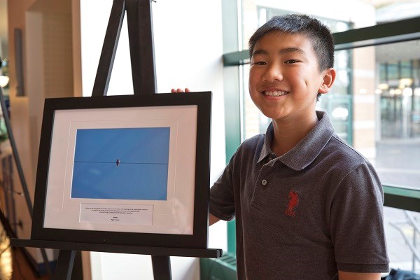 Young boy stands next to framed image on an easel with his arm around it.