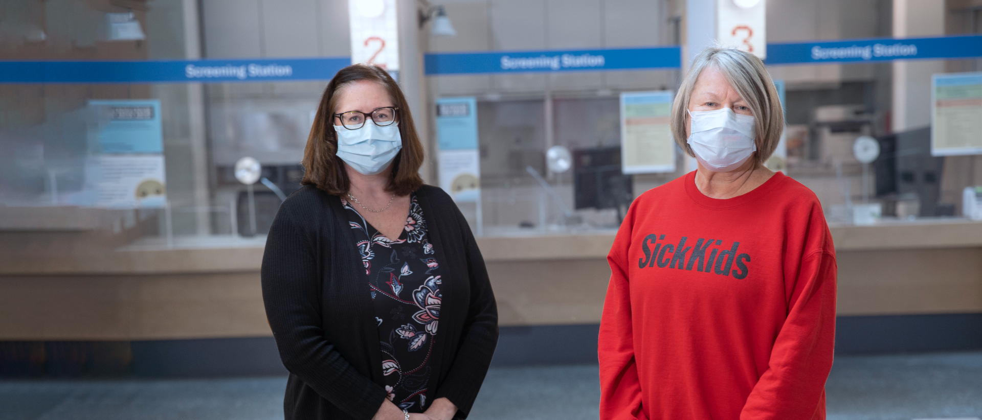 Stephanie Gracon-Lappan and Jane Ciordas-Lowes in masks. They are standing in front of the hospital screening stations. 