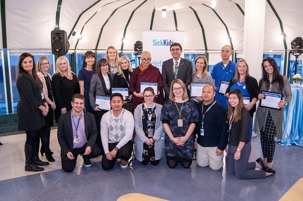 Group of staff stand together, some hold framed certificates.