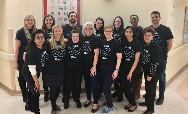 Team of staff stand together wearing all black and SickKids VS t-shirts.