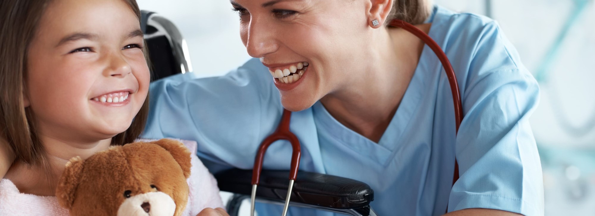smiling child holding a teddy bear laughing with her doctor