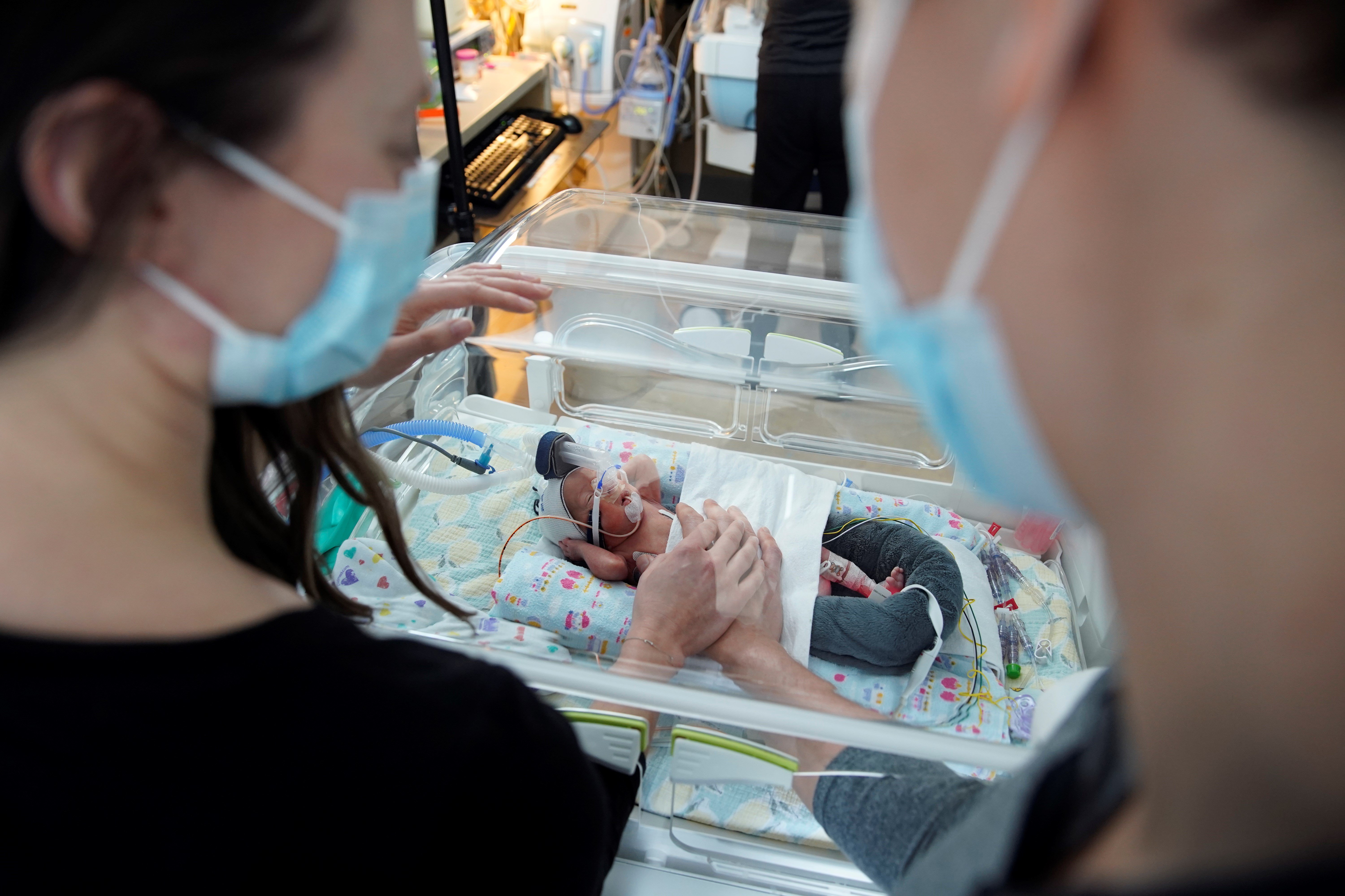 Erica and Brett in the SickKids NICU standing with Jeff in an incubator.
