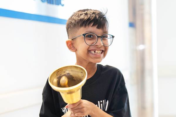 A child who is wearing glasses and smiling while ringing a handbell.