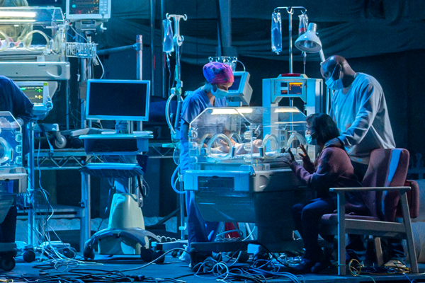 A nurse tending to a baby in an isolette (incubator) while the parents observe the baby through the glass.