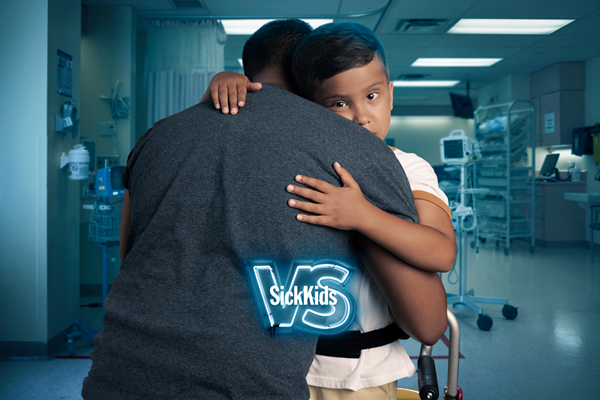 A child hugging an adult. The text reads, "Help build the new SickKids. Join the fight." Below, there is the SickKids VS logo and text that reads "Give monthly".
