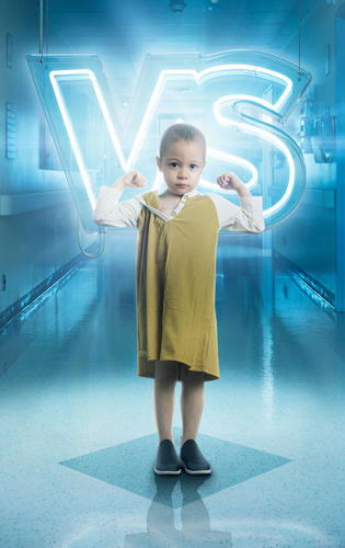 Small child standing in a hospital hallway flexing their arm muscles