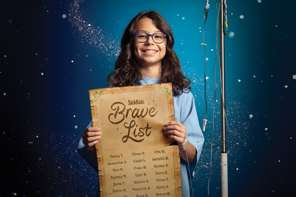 Child wearing glasses and holding a paper that reads "SickKids Brave List" and includes several names. The child has an IV pole.