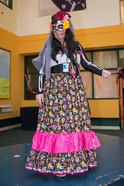 Woman dressed in a floral dress with skeletons on it and wearing skeleton makeup.