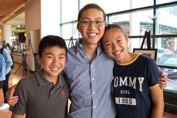 Three children stand with their arms around each other.