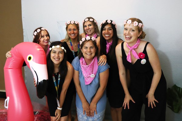 A group of adults wearing flower crowns pose with a blow up flamingo.