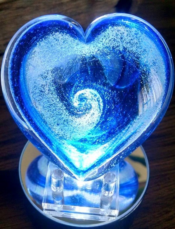 A glowing blue glass heart with ash design inside
