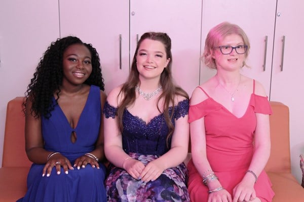 Three teens in formal attire sit side by side.