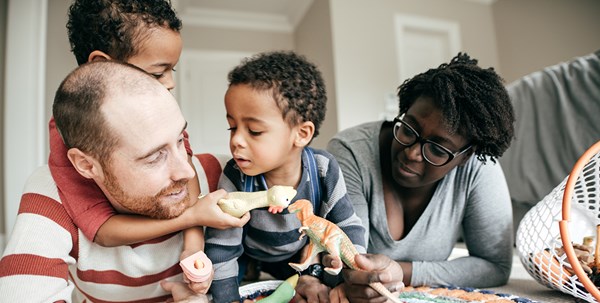 A family consisting of a man, woman and two children. The children are playing with dinosaur figures.