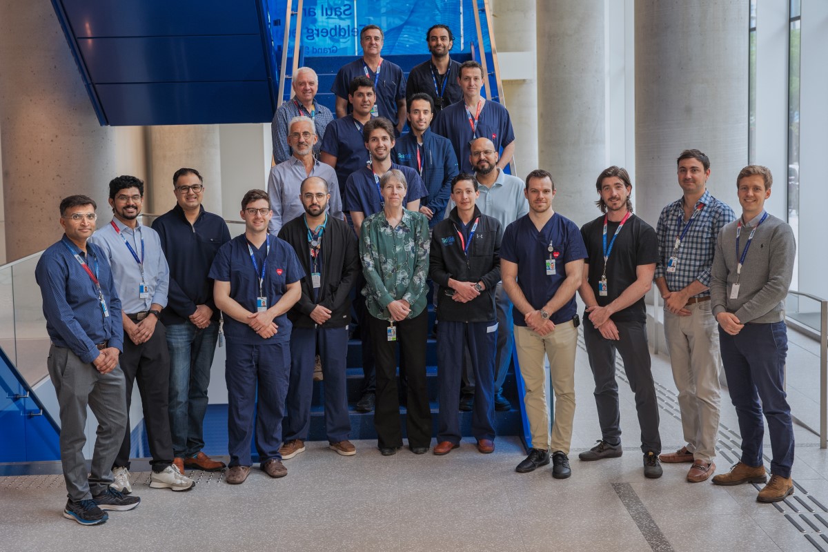 A large group of healthcare professionals wearing ID badges stands together on a staircase inside a modern hospital building.
