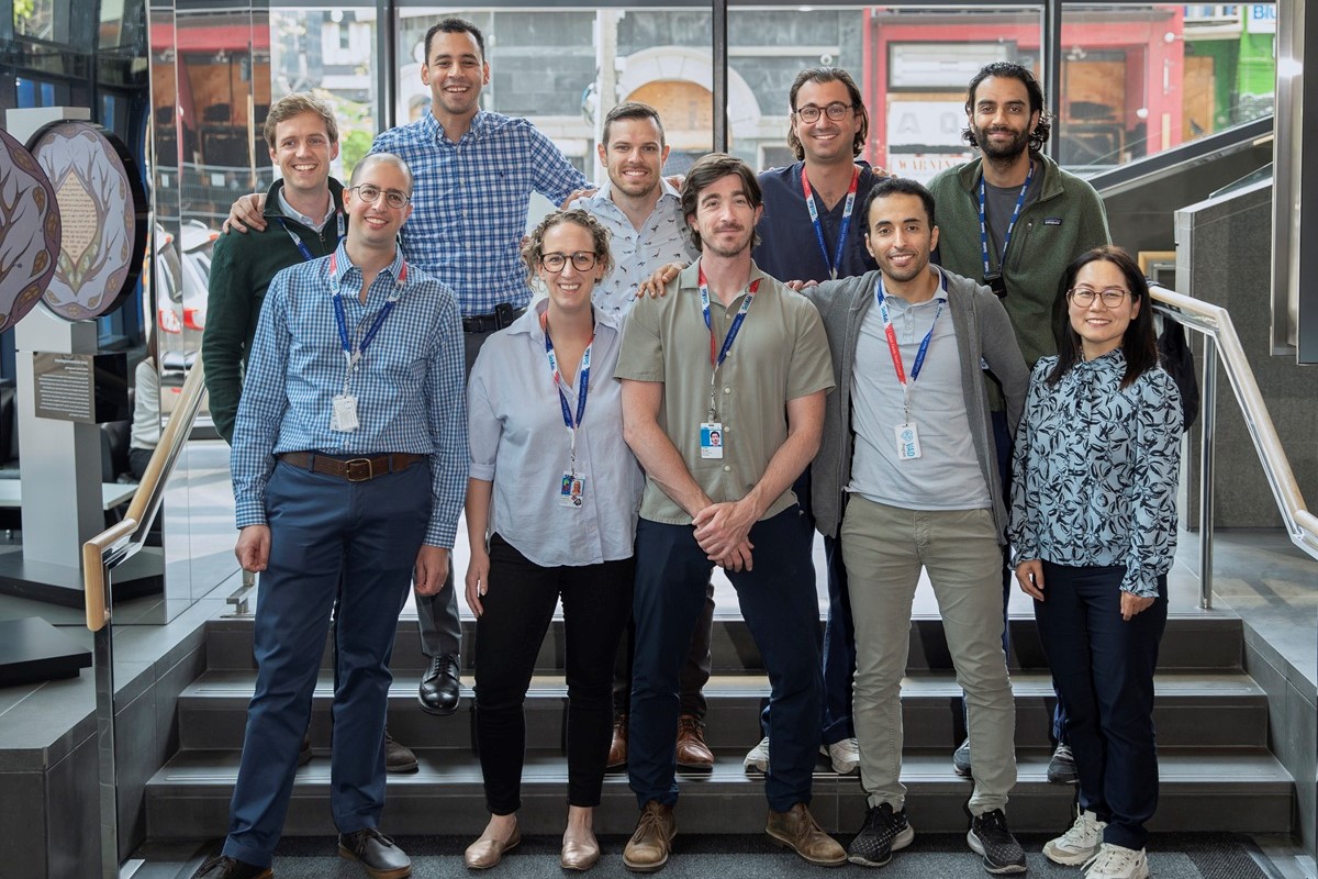 A group of nine people standing together on indoor steps, wearing business casual clothing and ID badges.