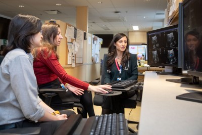 Two people sit with a clinician at a workstation, reviewing heart ultrasound images on computer screens in a clinical office.