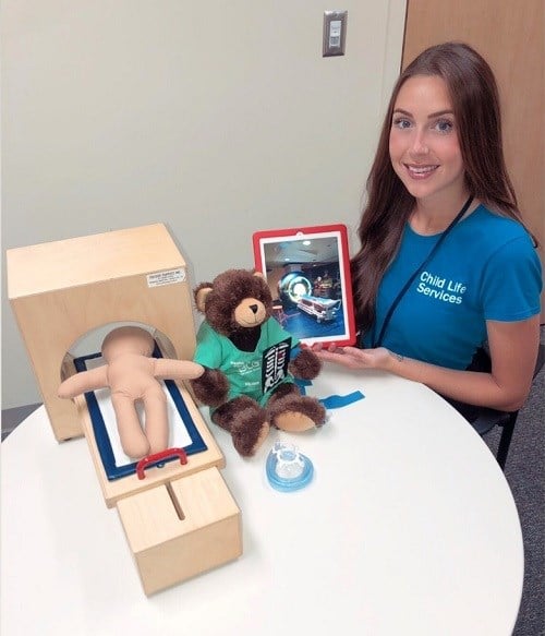 Person holds tablet showing an image of an MRI next to a table with MRI and medical related toys.