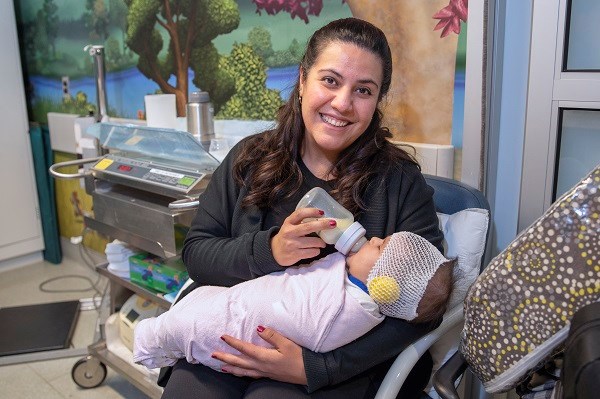 Woman feeds a bottle to an infant who is swaddled.