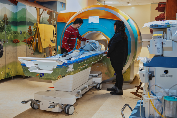 Two adults stand by while a baby is in an MRI scanner.