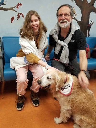 Teen girl sits with an adult and a golden retriever.