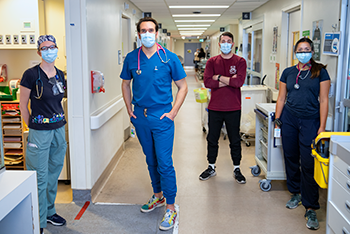Four nurses wearing medical masks stand in a crowded hospital hallway.