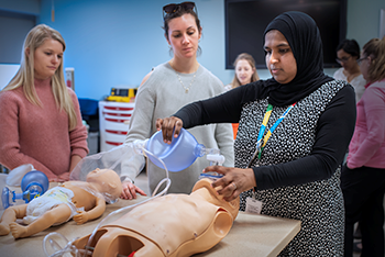 Woman demonstrates a medical procedure on a simulation device. Two women observe.