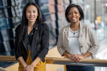 Two women wearing business casual clothing smile at the camera.