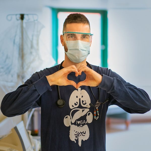 Man wearing face mask forms a heart with his hands.