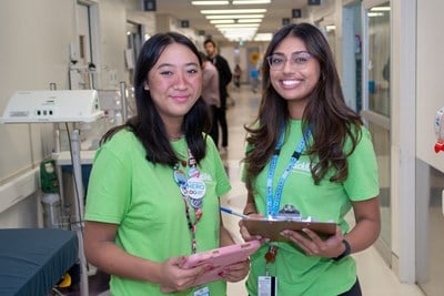 Two people stand in a hospital hallway holding tablets.