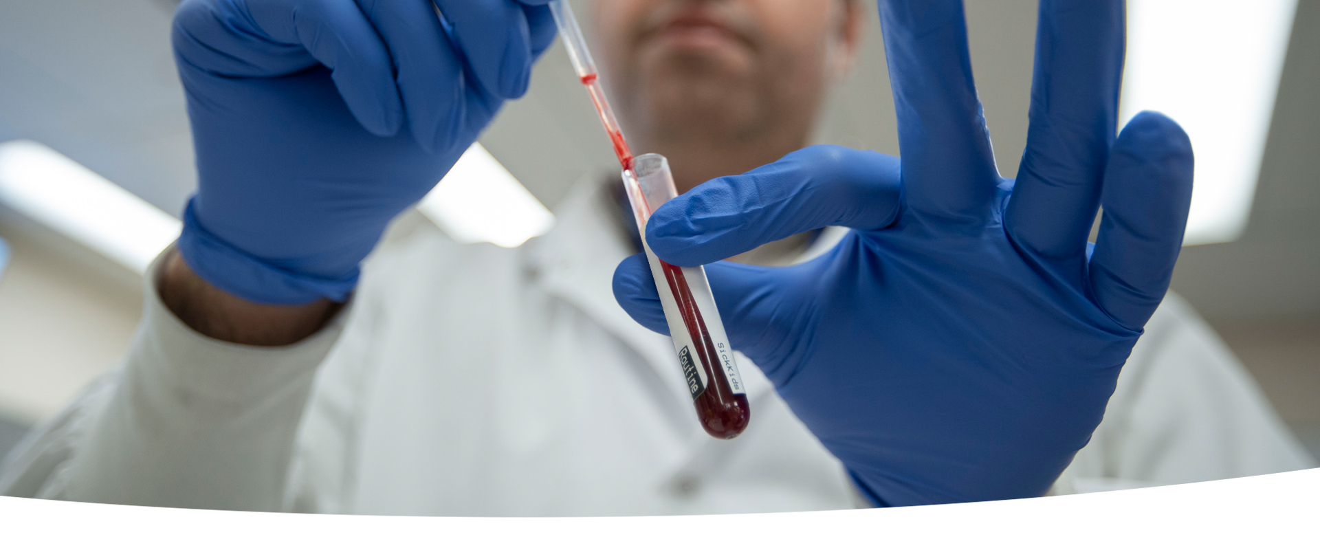 A closeup of gloved hands pipetting from a blood sample in a glass tube.