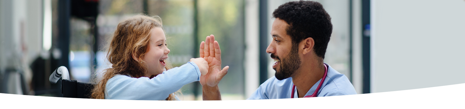 A child in a wheelchair smiling and interacting with a hospital staff member