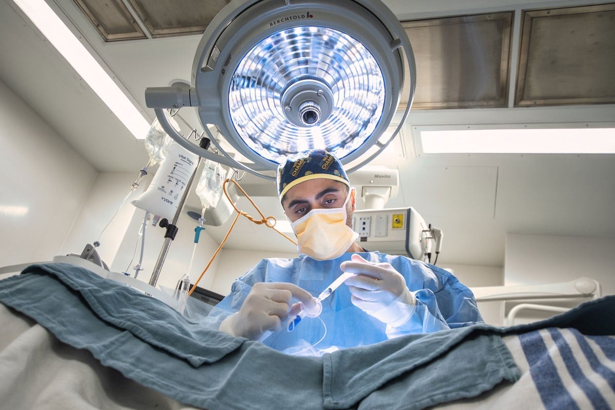 Surgeon wearing mask and holding instruments over operating table.