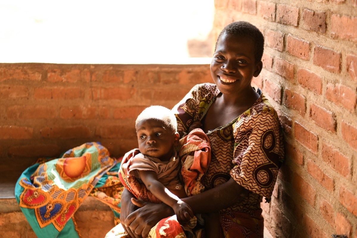 A mother smiling while holding a baby swaddled in a patterned cloth.