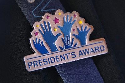 The President's Award pin, attached to a SickKids lanyard. The pin features five hands reaching upward to the stars.