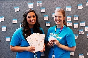 Two staff stand in front of a bulletin board filled with small hand written notes